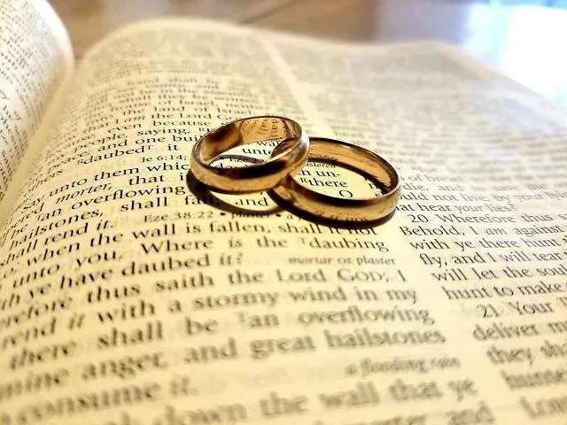 SC Corina Spriestersbach - Freie Rednerin - Zwei goldene Eheringe liegen auf einer offenen Bibel mit verschwommenem Text im Hintergrund