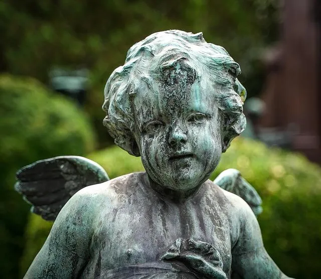 SC Corina Spriestersbach - Freie Rednerin - Nahaufnahme einer verwitterten Bronze-Cherub-Statue mit Flügeln im Freien