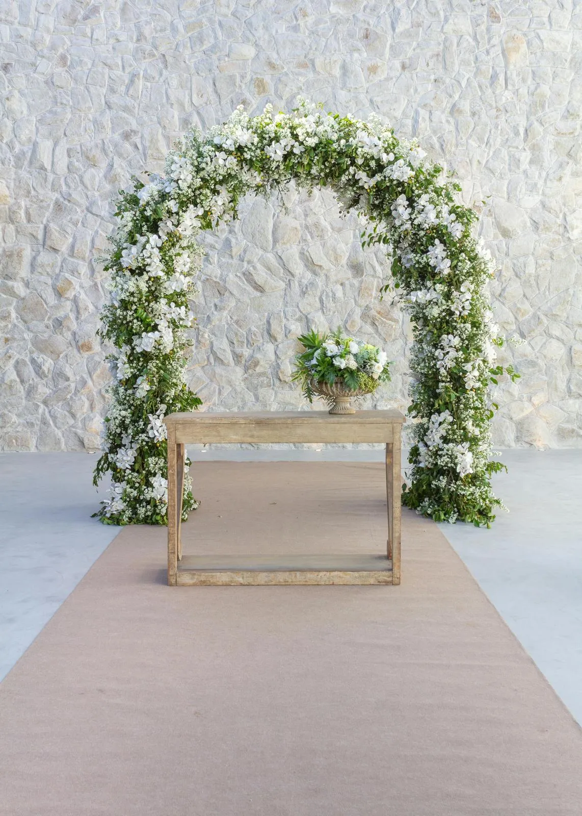 SC Corina Spriestersbach – Freie Rednerin – Holztisch mit Blumenarrangement vor einem weiß-grünen Blumenbogen vor einer Steinmauer