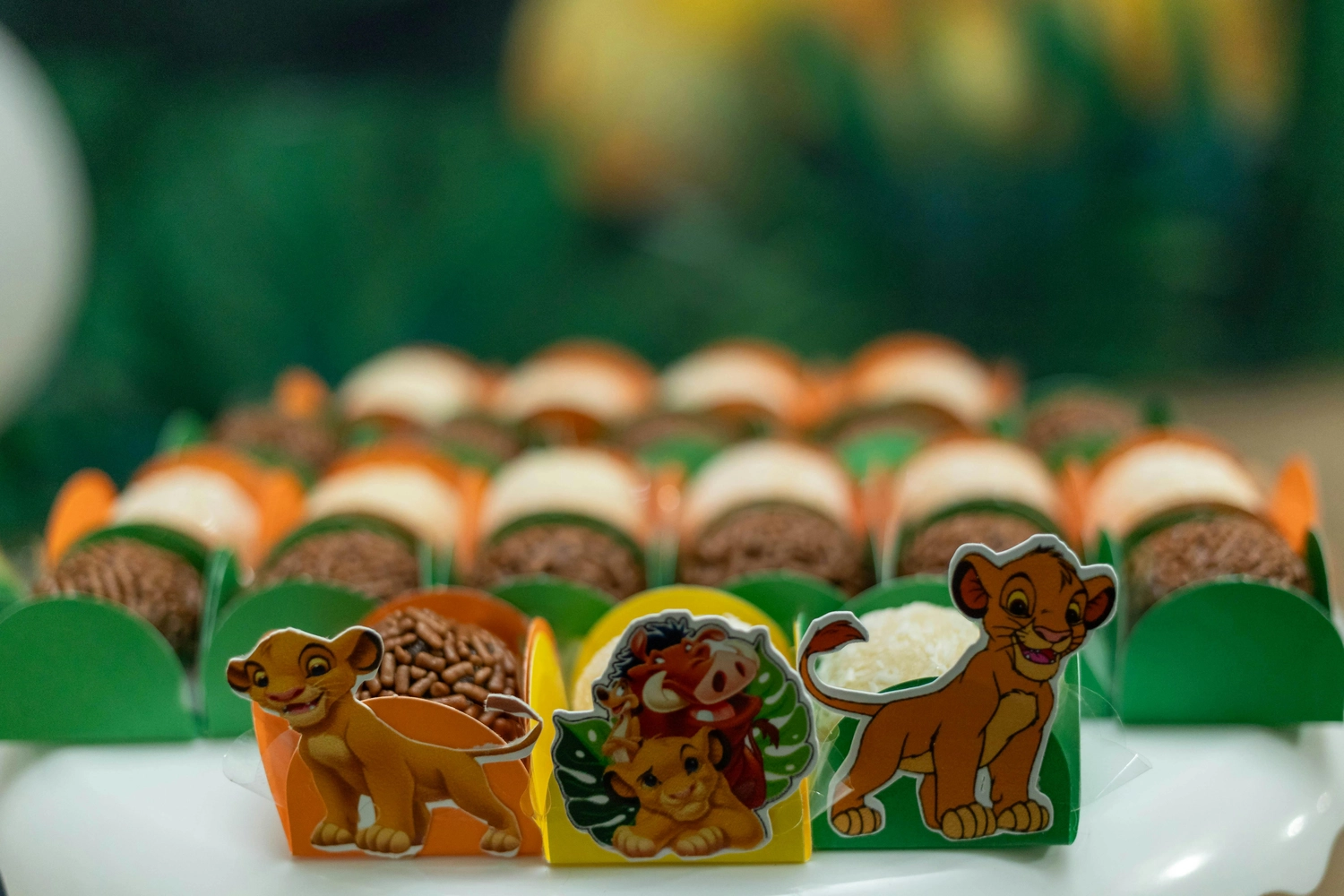 SC Corina Spriestersbach - Freie Rednerin - Reihen von verschiedenen Schokoladen- und Kokosnuss-Brigadeiros in farbenfrohen Verpackungen, verziert mit den Zeichentrickfiguren Simba, Timon und Pumbaa aus König der Löwen